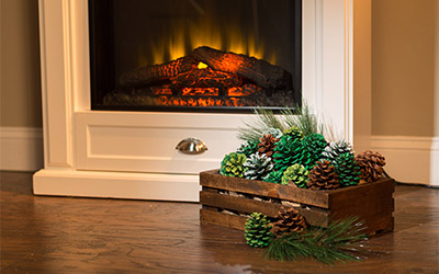 Glittery pine cones arranged in a wood crate near fireplace.