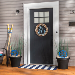 A front porch with nautical décor, including an anchor wreath on the front door and wooden oars next to the door. 