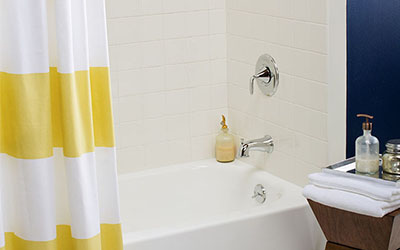 A white bathtub with a white tile wall and yellow and white striped shower curtain.